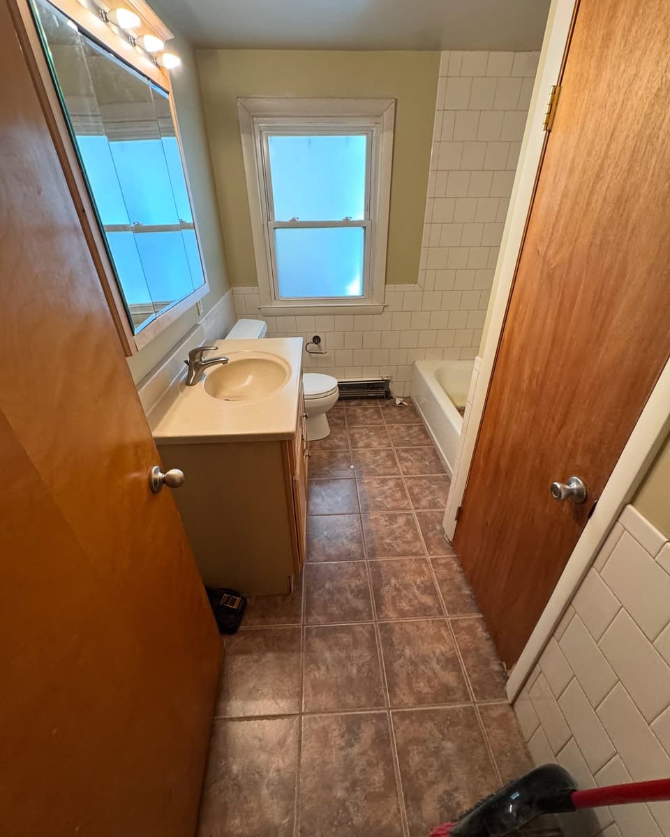 Bathroom before: brown tile floor, a dated vanity and a wood door