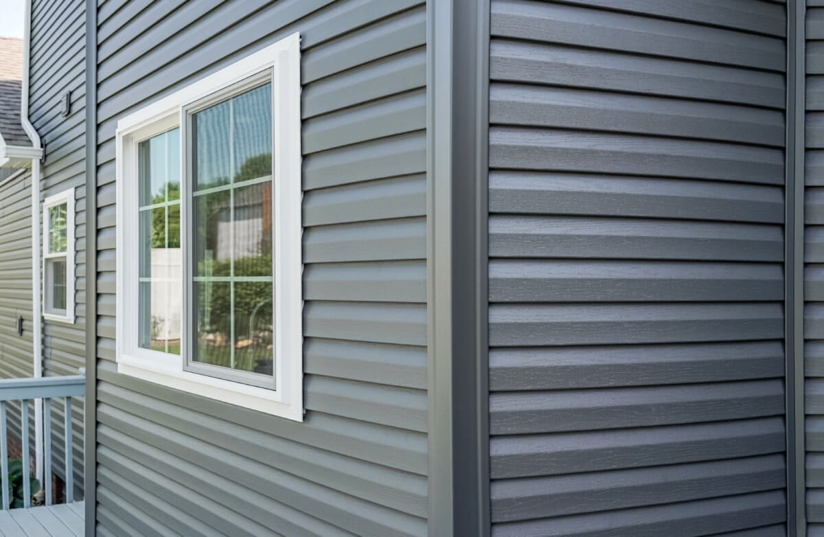 Siding installation by Farley Construction — gray vinyl siding with white window trim on a home’s exterior corner